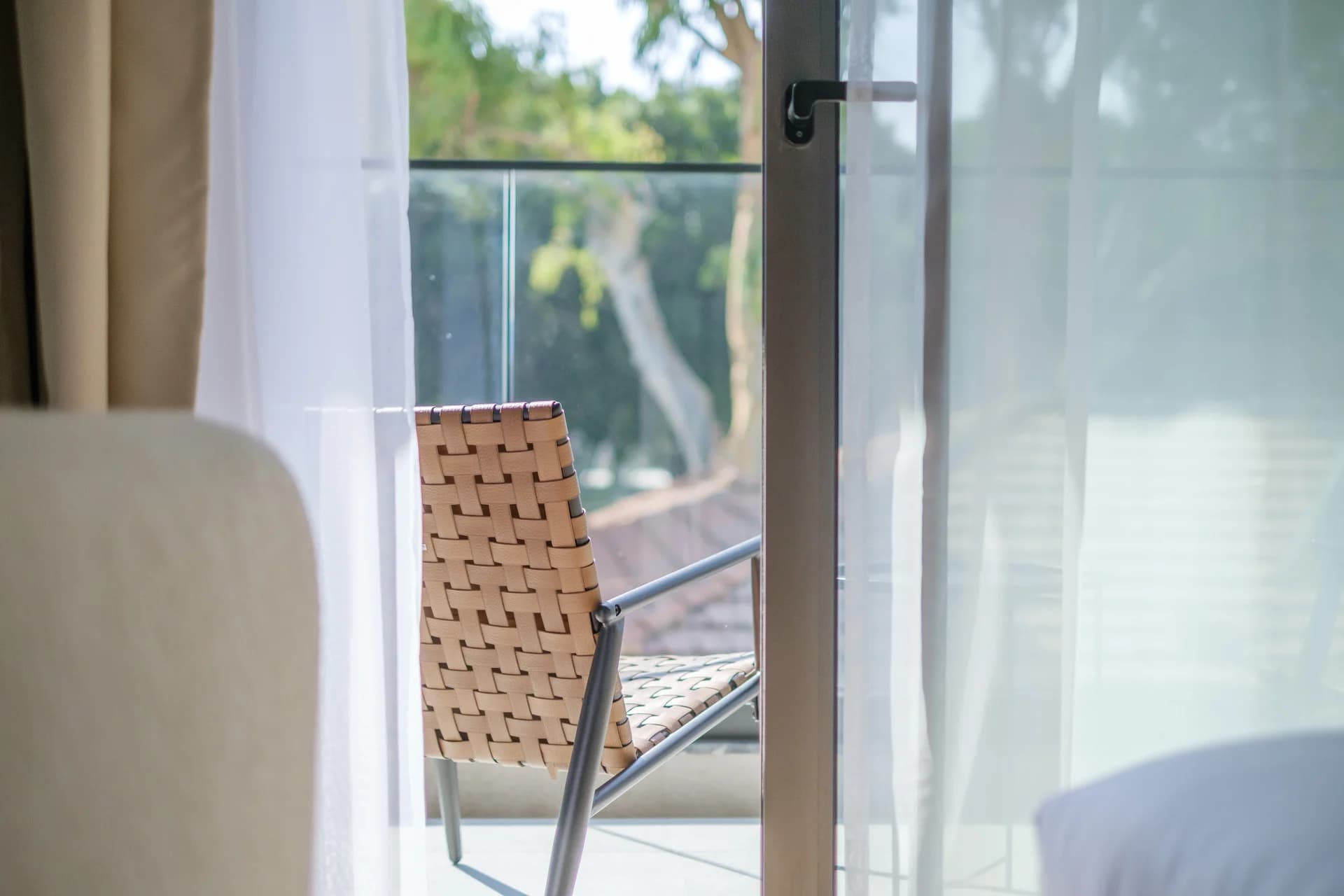 Woven chair on a STAY 1 balcony seen through sheer curtains