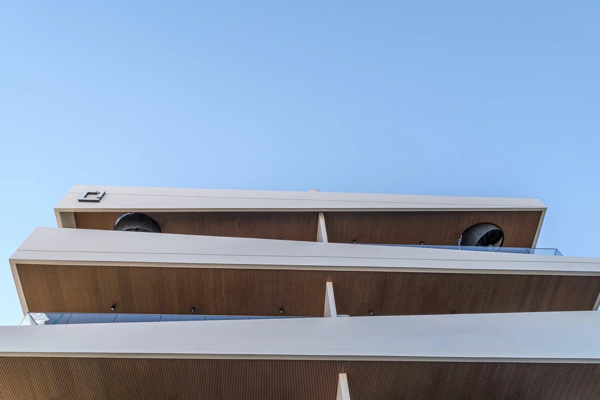 Looking up at URBN's white balconies with timber soffits against a blue sky