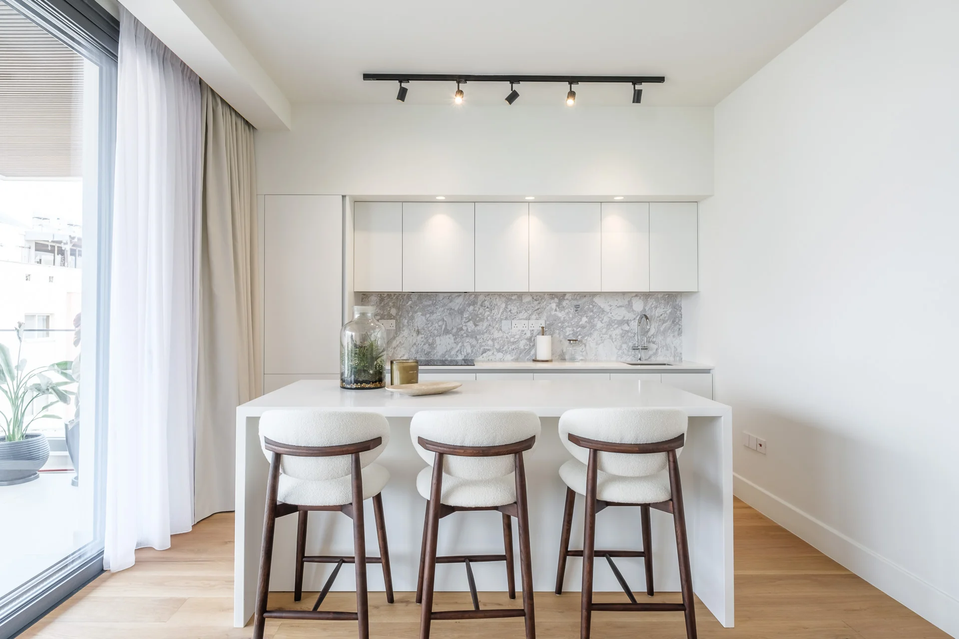 URBN kitchen with a white island, marble splashback and three bar stools