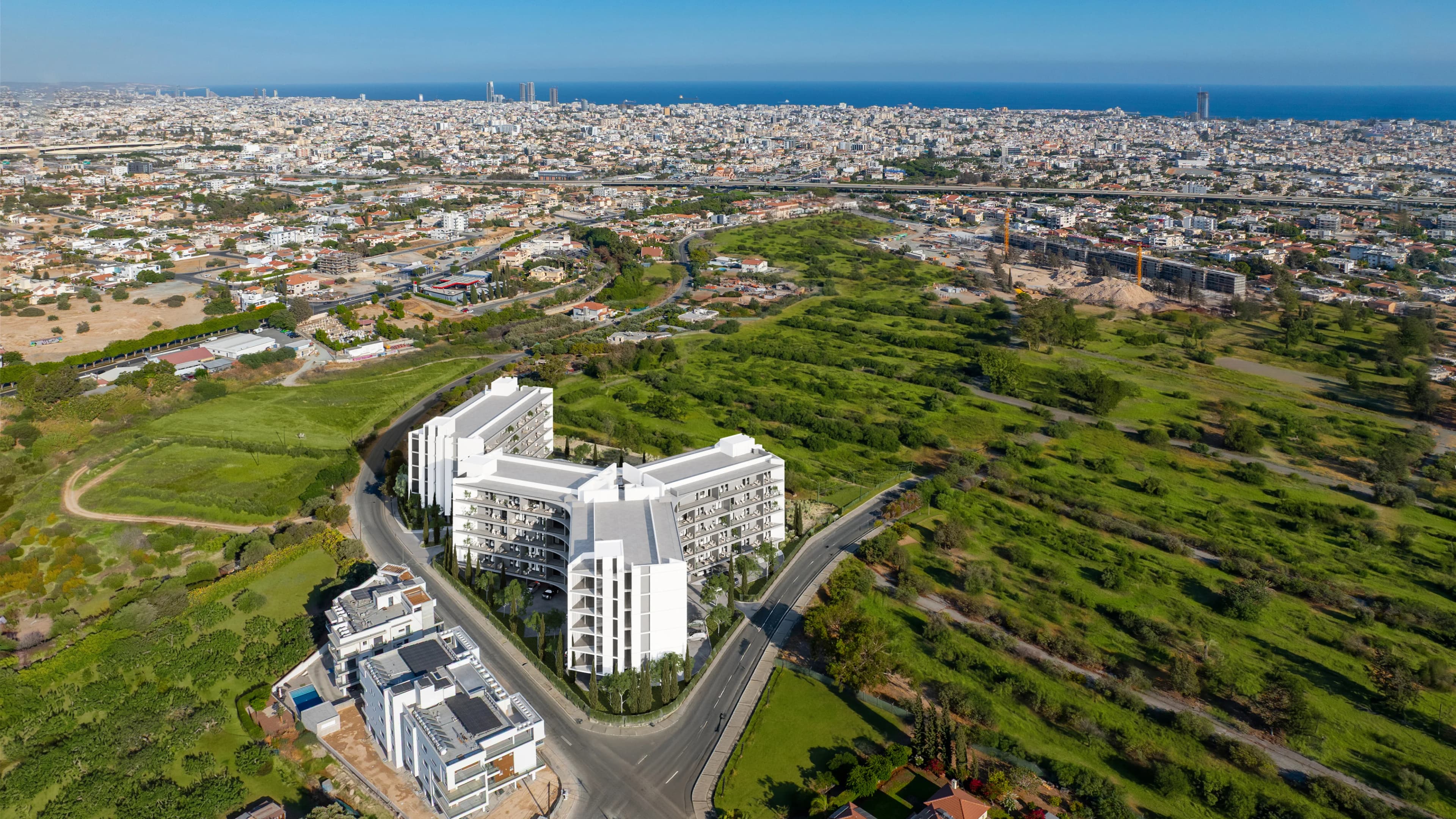 Aerial view of ZOIA's white blocks among green fields in Kato Polemidia, with Limassol and the sea beyond