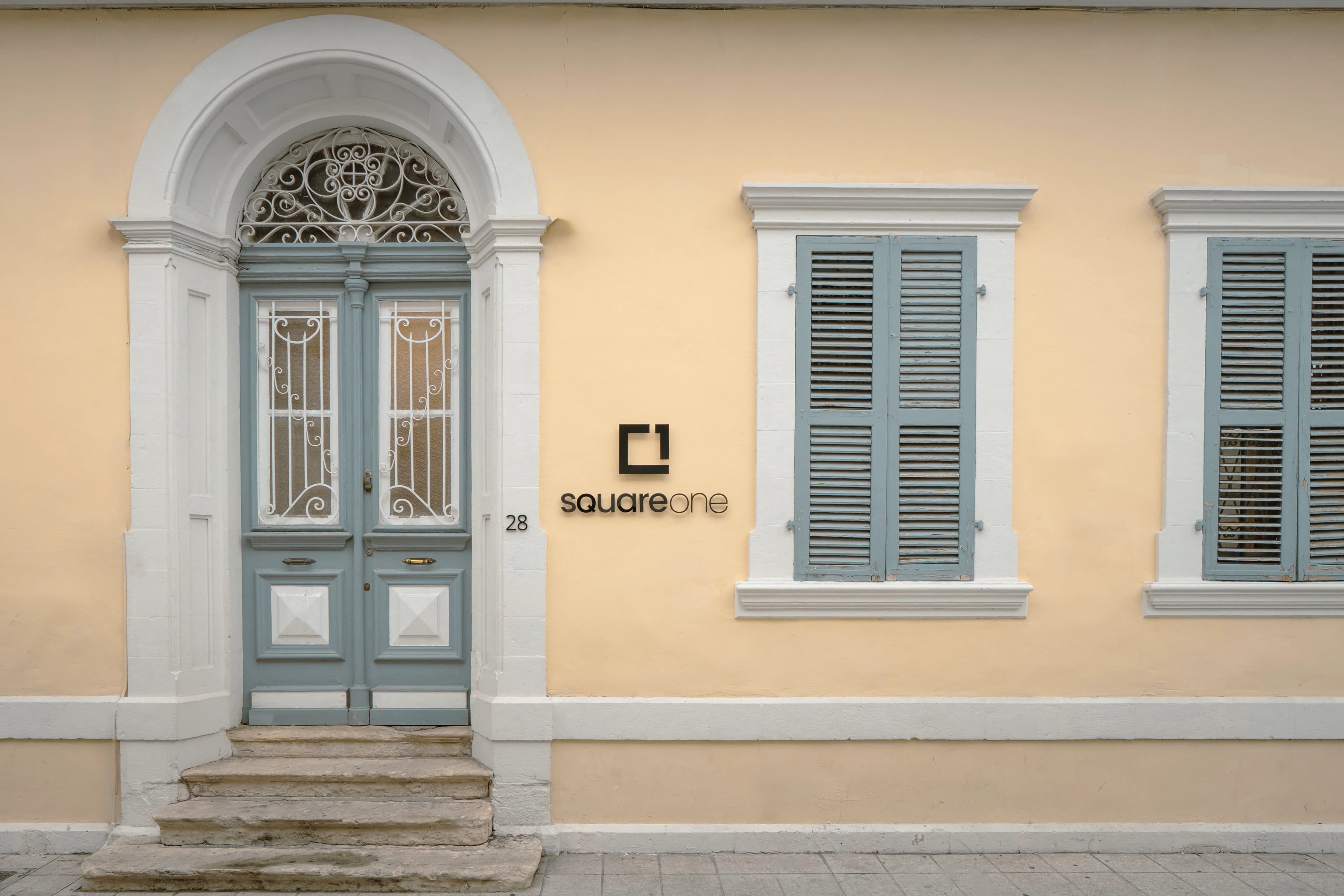The arched blue front door of SquareOne's office, its logo on the pale yellow wall beside it
